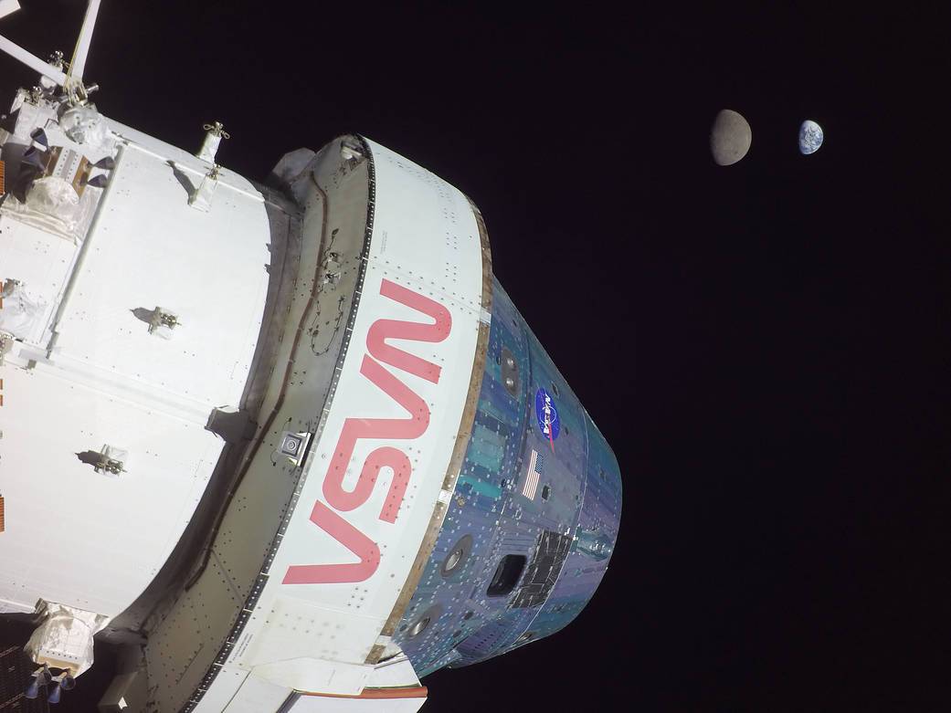 Orion in the foreground with the Moon and Earth visible in the black sky during Artemis I